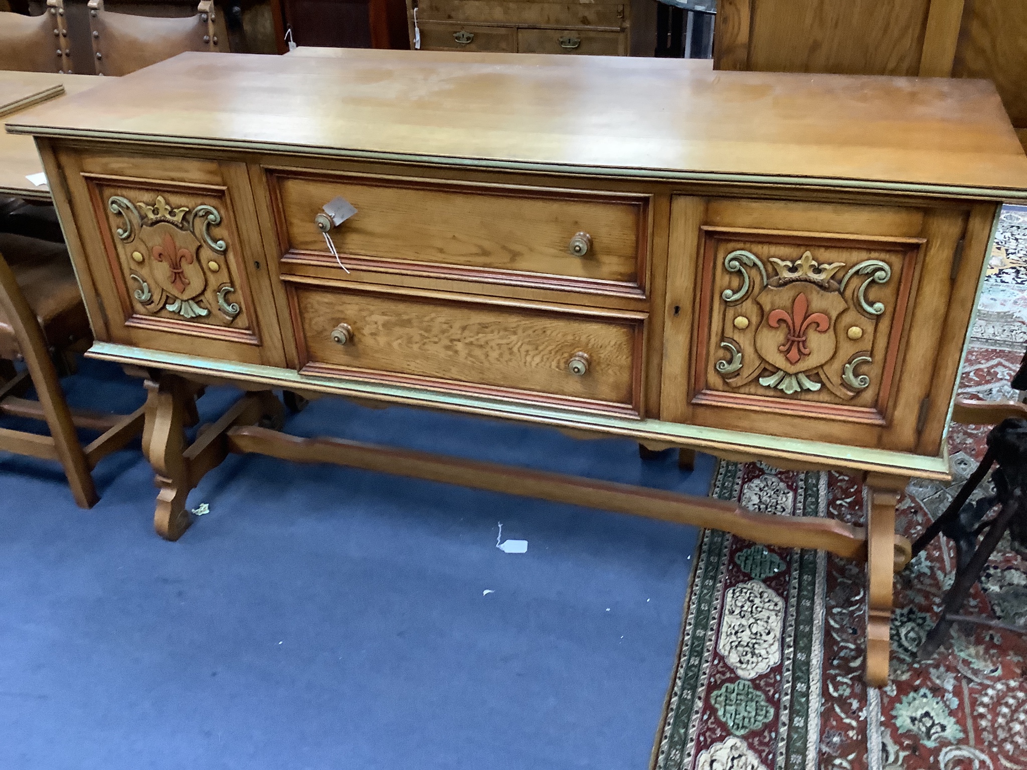 A Maple & Co oak dining suite of Italianate design, with carved and painted decoration and heraldic panels, comprising refectory table, six studded hide-covered chairs, sideboard, two-door cabinet on stand and a side tab